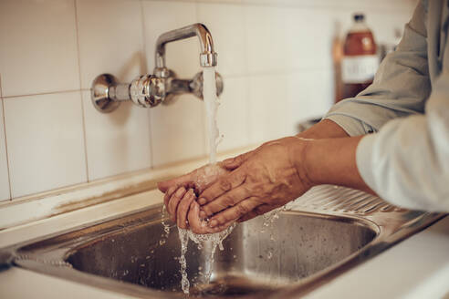 Nahaufnahme einer Frau, die sich am Küchenbecken die Hände mit Wasser und Seife wäscht - ACPF00710