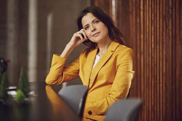 Portrait of businesswoman wearing yellow suit sitting at desk in office - MCF00731