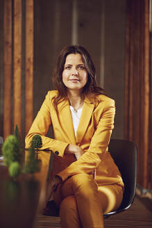 Portrait of businesswoman wearing yellow suit sitting at desk in office - MCF00738