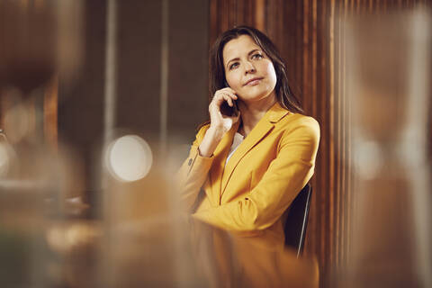 Geschäftsfrau am Telefon im gelben Anzug sitzt am Schreibtisch im Büro, lizenzfreies Stockfoto