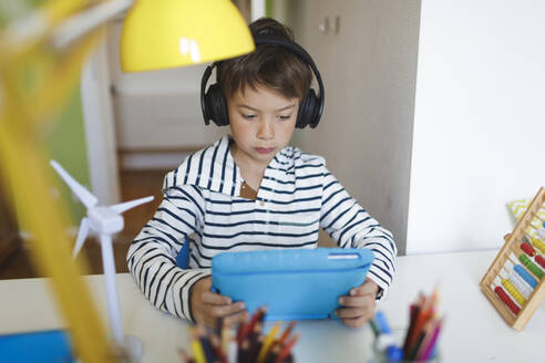 Boy doing homeschooling and using tablet and headphones at home - HMEF00894
