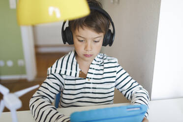 Boy doing homeschooling and using tablet and headphones at home - HMEF00895
