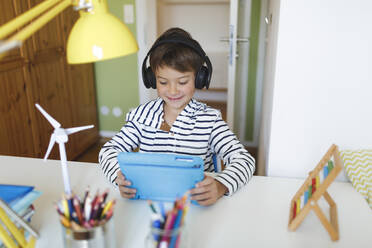 Boy doing homeschooling and using tablet and headphones at home - HMEF00896