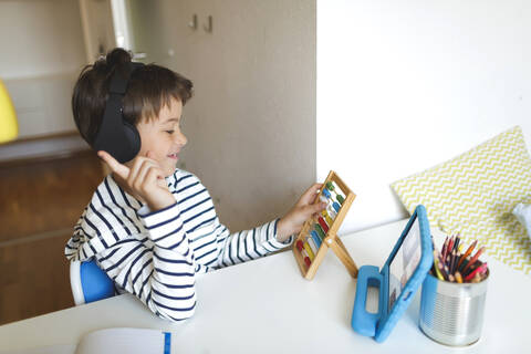 Boy doing homeschooling and using slide rule, tablet and headphones at home stock photo