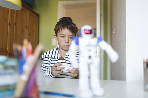 Boy playing with his remote-controlled toy robot at home - HMEF00910