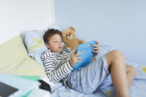 Boy lying in bed using digital tablet - HMEF00914