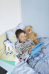 Boy lying in bed using digital tablet - HMEF00915