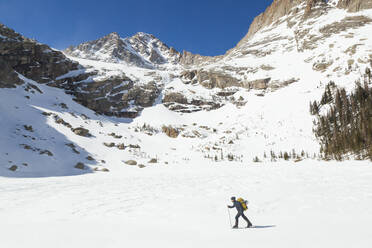 Woman hikes across frozen Black Lake, Rocky Mountain National Park - CAVF79094