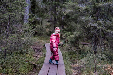 Girl smiling walking along a boardwalk in a forest in winter - CAVF79218