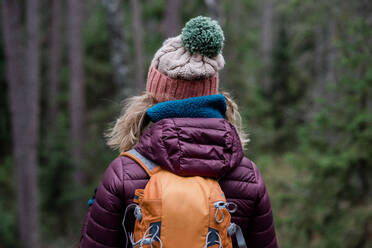 Rücken einer Frau, die im Winter in einem Wald steht und mit einem Rucksack wandert - CAVF79219
