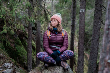 Frau sitzt auf einem Felsen und denkt beim Wandern im Wald in Schweden nach - CAVF79224