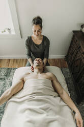Lächelnde Massagetherapeutin behandelt den Nacken eines männlichen Patienten - CAVF79243