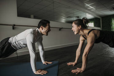 Fit male and female friends smile and do pushups together in a gym - CAVF79255