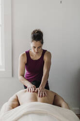 Eine weibliche Masseurin behandelt den Rücken eines männlichen Patienten mit ihren Händen - CAVF79257