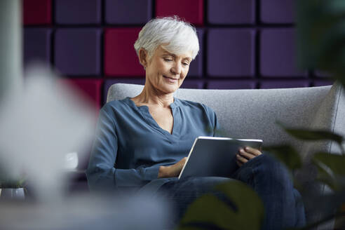 Porträt einer älteren Geschäftsfrau, die auf einem Liegestuhl sitzt und ein digitales Tablet benutzt - RBF07566