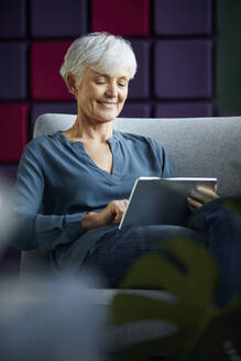 Porträt einer lächelnden älteren Geschäftsfrau, die auf einem Liegestuhl sitzt und ein digitales Tablet benutzt - RBF07567