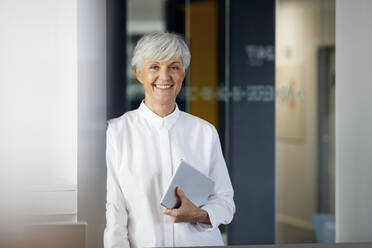 Portrait of smiling senior businesswoman with digital tablet in an office - RBF07582