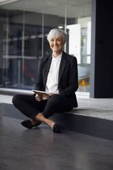 Porträt einer eleganten älteren Geschäftsfrau, die auf einer Stufe im Büro sitzt - RBF07595