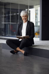 Porträt einer eleganten älteren Geschäftsfrau, die auf einer Stufe im Büro sitzt - RBF07596