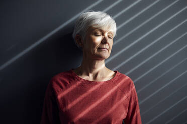 Porträt einer älteren Frau mit geschlossenen Augen, die an der Wand lehnt - RBF07604