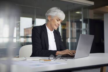 Ältere Geschäftsfrau sitzt am Schreibtisch und arbeitet am Laptop - RBF07612