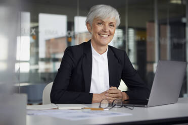 Porträt einer lächelnden älteren Geschäftsfrau, die am Schreibtisch im Büro sitzt - RBF07613