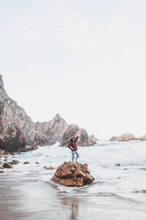 Junge Frau steht mit erhobenem Arm auf einem Felsen, Praia da Ursa, Lisboa, Portugal - FVSF00190