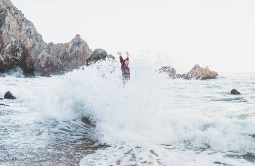 Junge Frau steht auf einem Felsen mit einer großen Welle, Praia da Ursa, Lisboa, Portugal - FVSF00192