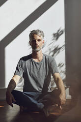 Portrait of mature man sitting on the floor at home meditating - MCF00778