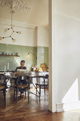 Mature man sitting in kitchen reading newspaper - MCF00782