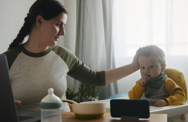 Mother stroking baby boy watching movies on mobile phone - BZF00547