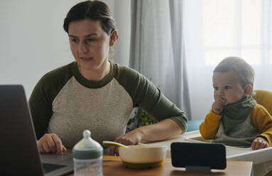 Mutter und kleiner Sohn schauen zusammen am Laptop zu Hause - BZF00549