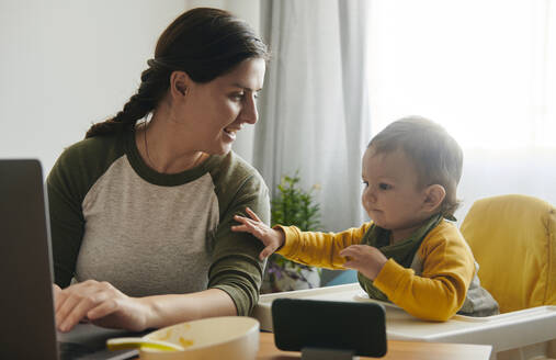 Mutter arbeitet am Laptop und beobachtet ihren kleinen Sohn - BZF00550