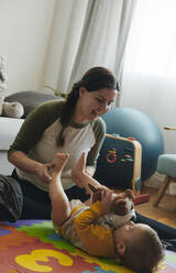 Mother playing with her little son on floor of the living room - BZF00551