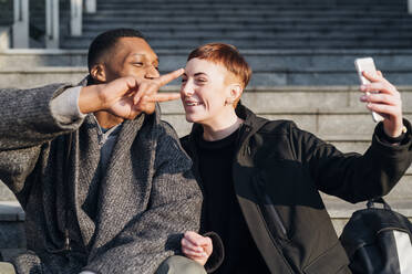 Junges Paar sitzt auf einer Treppe in der Stadt und macht ein Selfie - MEUF00417