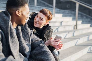 Happy young couple in the city sitting on stairs with cell phone - MEUF00420