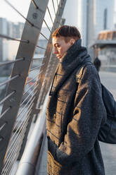 Porträt einer rothaarigen jungen Frau auf einer Brücke in der Stadt bei Sonnenuntergang - MEUF00462
