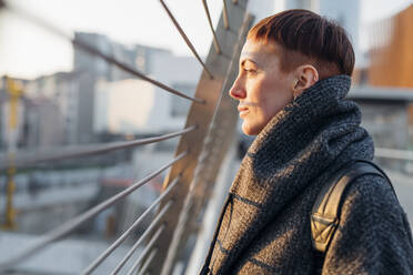 Porträt einer rothaarigen jungen Frau auf einer Brücke in der Stadt bei Sonnenuntergang - MEUF00464