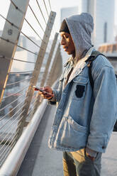Young man standing on a bridge in the city using smartphone - MEUF00465