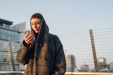 Redheaded young woman using smartphone on a bridge in the city - MEUF00469