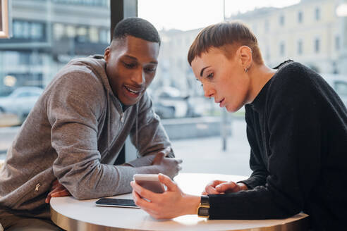 Junges Paar teilt sich ein Smartphone in einem Café - MEUF00474