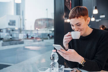 Rothaarige junge Frau benutzt Smartphone in einem Café - MEUF00481