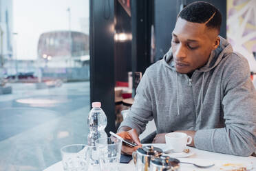 Junger Mann benutzt Smartphone in einem Café - MEUF00483
