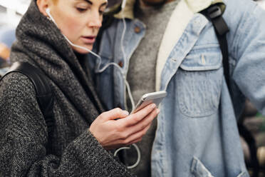 Junges Paar mit Ohrstöpseln und Smartphone in einer U-Bahn - MEUF00511