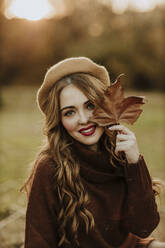 Portrait of fashionable woman with autumn leaf at backlight - GMLF00080