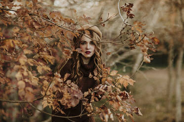 Porträt einer modischen Frau, die hinter Herbstblättern steht - GMLF00084