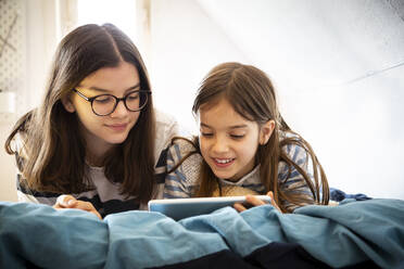 Sisters using tablet lying on bed - LVF08846