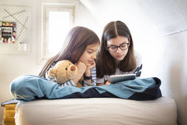 Sisters using tablet lying on bed - LVF08847