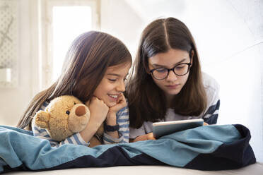 Sisters using tablet lying on bed - LVF08848