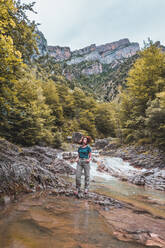 Spain, Province of Huesca, Portrait of female hiker posing over clear mountain river - FVSF00204